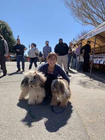 Deidre kneeling between Cookie and Turtle outdoors at a dog show