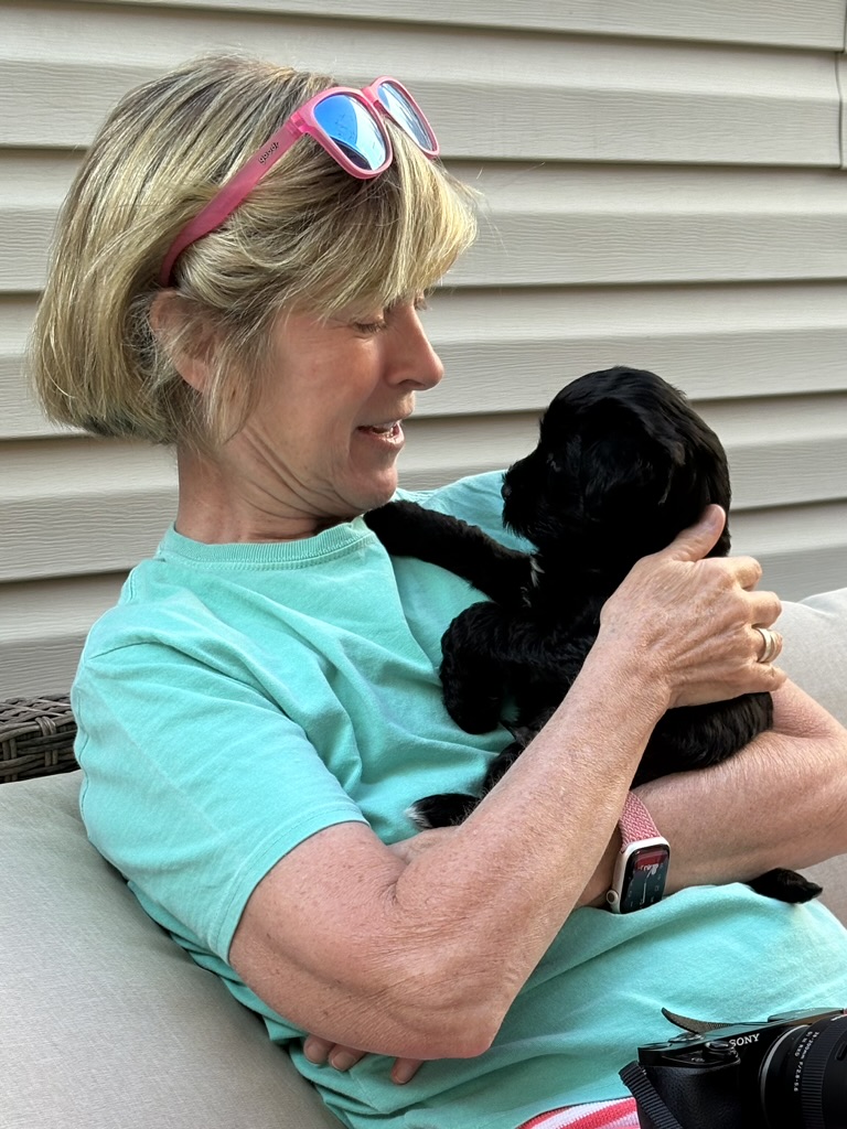 A visitor snuggling a black puppy on the patio