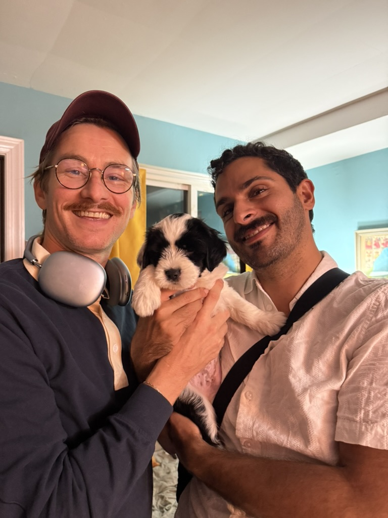 Two visitors smiling with a black-and-white puppy held between them