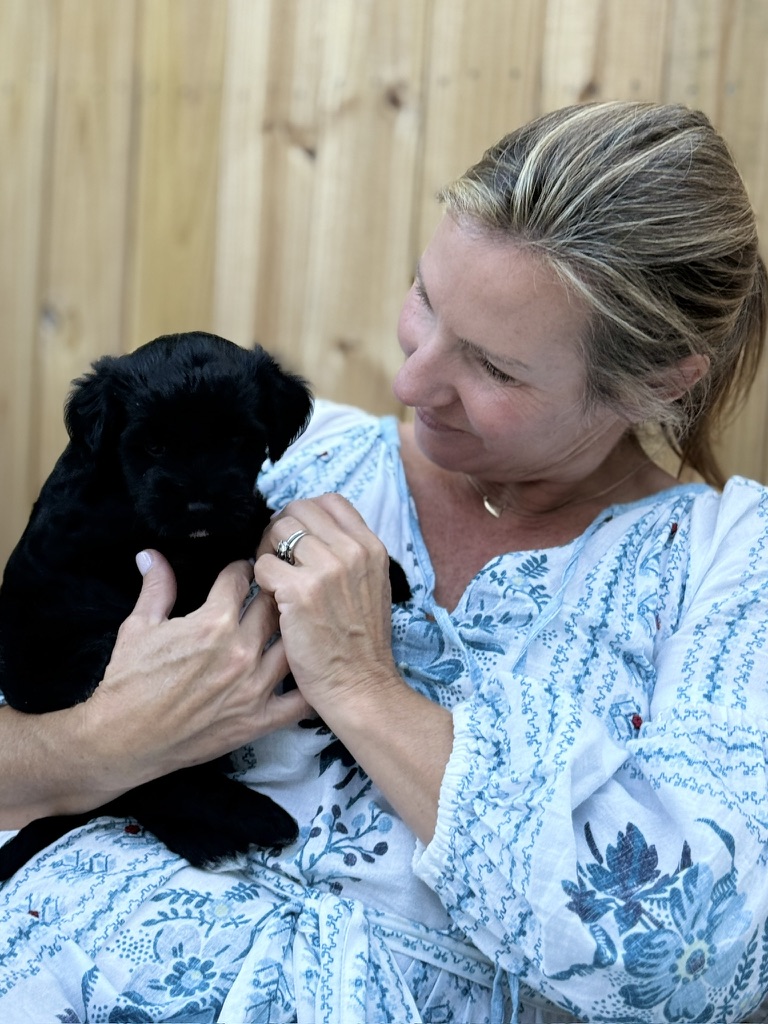 A woman in a floral top holding a young black puppy outdoors